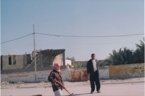 Iraqi man wearing red checkered keffiyeh, holding a shovel and another Iraqi man standing nearby.